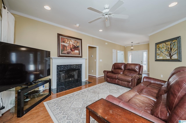 living room with wood-type flooring, ornamental molding, a premium fireplace, and ceiling fan