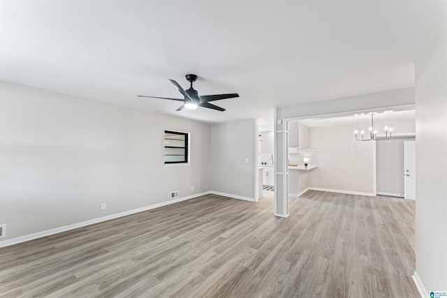 unfurnished living room with ceiling fan with notable chandelier and light hardwood / wood-style floors