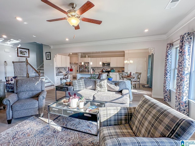 living room with ornamental molding, ceiling fan with notable chandelier, and light hardwood / wood-style floors