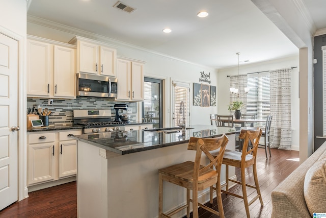 kitchen featuring dark wood-type flooring, a kitchen island with sink, dark stone countertops, stainless steel appliances, and ornamental molding