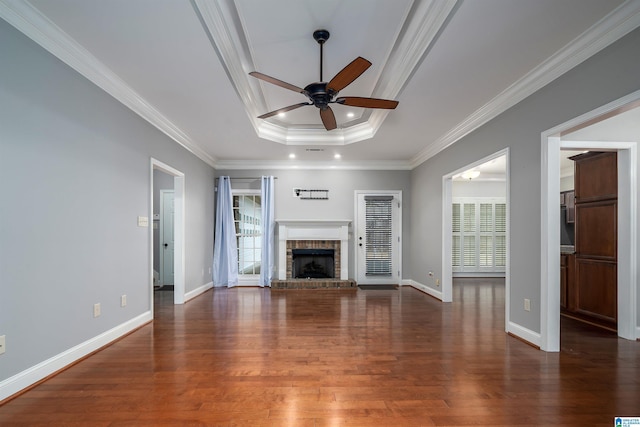 unfurnished living room with dark hardwood / wood-style floors, ceiling fan, a tray ceiling, crown molding, and a brick fireplace