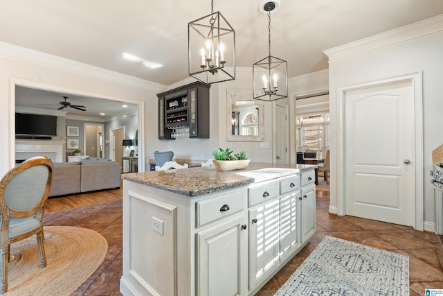 kitchen featuring pendant lighting, white cabinets, ornamental molding, a center island, and light stone counters