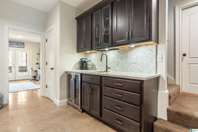 bar featuring french doors, dark brown cabinetry, sink, beverage cooler, and decorative backsplash