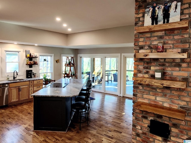 kitchen featuring a kitchen island, sink, a kitchen bar, hardwood / wood-style flooring, and light stone countertops