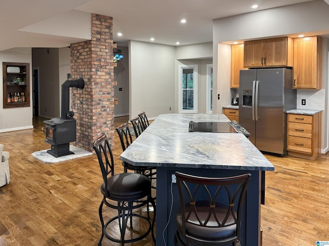 kitchen with a wood stove, light stone countertops, a kitchen bar, stainless steel fridge with ice dispenser, and light wood-type flooring