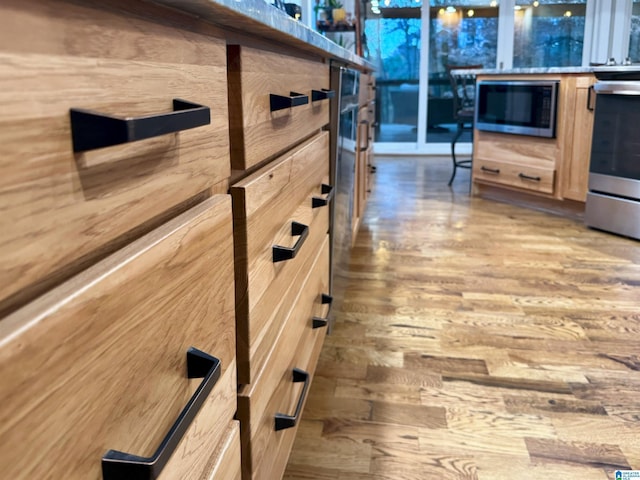 details with appliances with stainless steel finishes, light brown cabinetry, and wood-type flooring