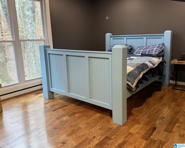 bedroom featuring baseboard heating, multiple windows, and light hardwood / wood-style flooring