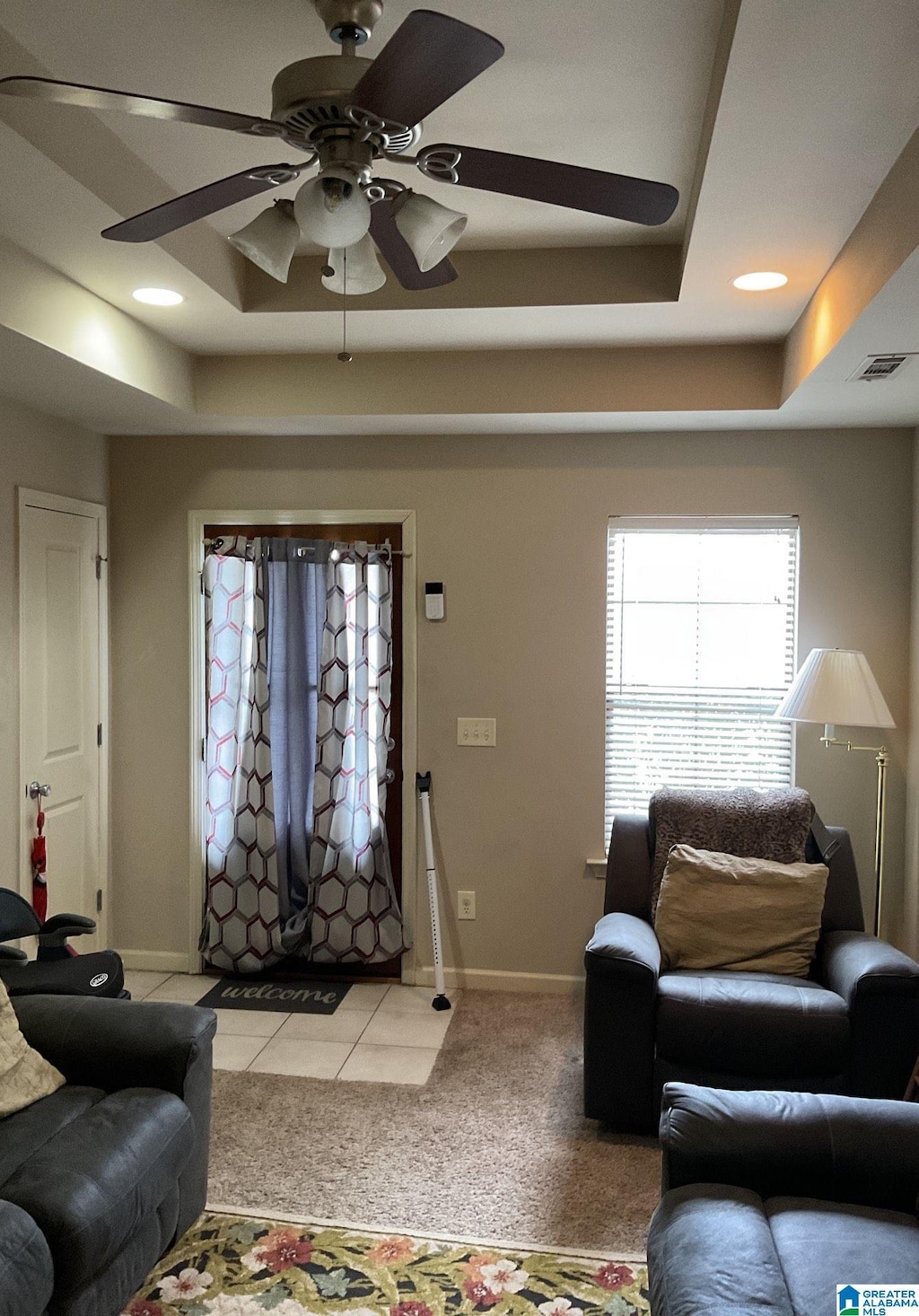 living area with light colored carpet, a raised ceiling, visible vents, and baseboards