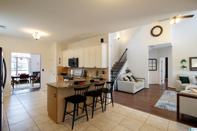 kitchen featuring light tile patterned floors, a breakfast bar area, white cabinetry, dark stone countertops, and kitchen peninsula