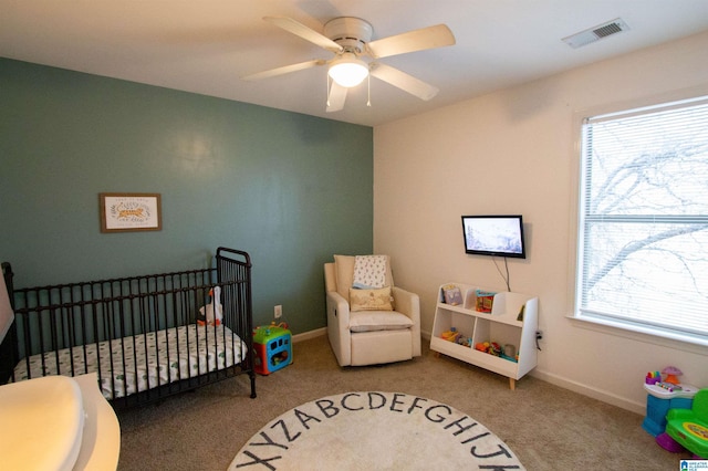 bedroom with multiple windows, carpet, a crib, and ceiling fan