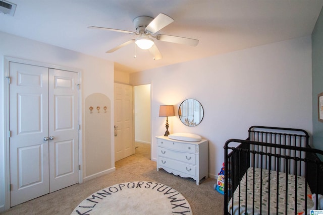 bedroom featuring a crib, light carpet, ceiling fan, and a closet