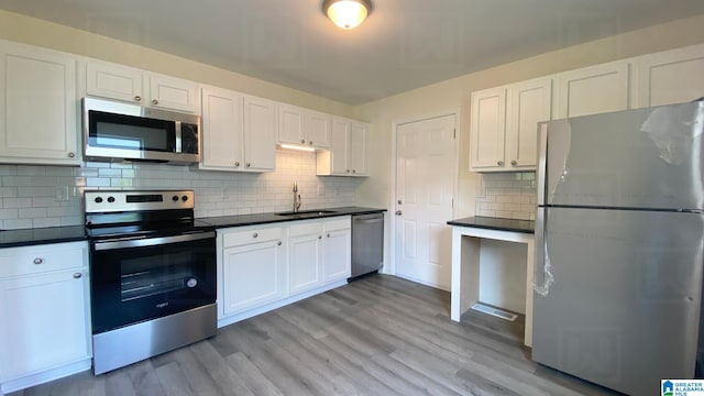 kitchen featuring appliances with stainless steel finishes, white cabinetry, sink, decorative backsplash, and light wood-type flooring