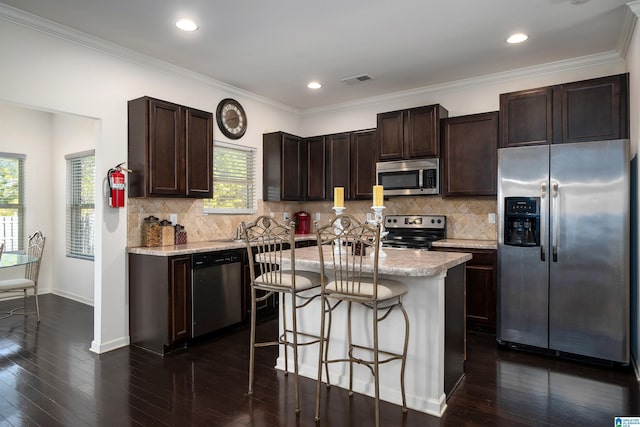 kitchen featuring crown molding, dark wood-type flooring, stainless steel appliances, light stone countertops, and a kitchen island