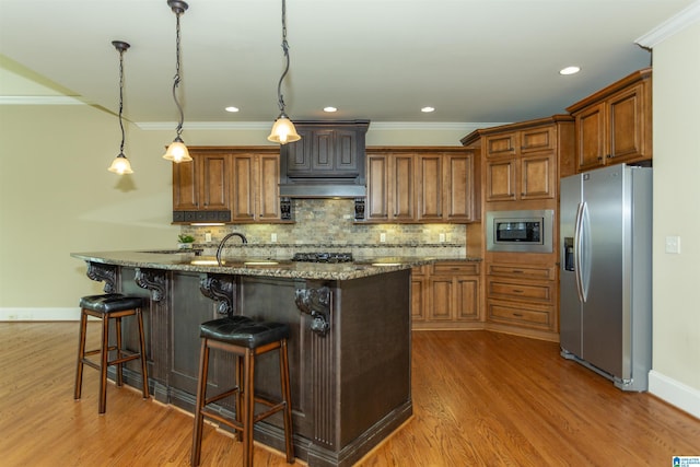 kitchen featuring appliances with stainless steel finishes, hanging light fixtures, an island with sink, and light stone counters