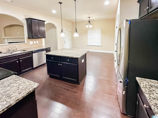 kitchen with light stone counters, hanging light fixtures, a kitchen island, stainless steel appliances, and decorative backsplash