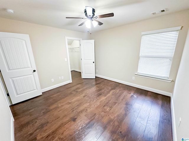 unfurnished bedroom with a walk in closet, dark hardwood / wood-style floors, and ceiling fan