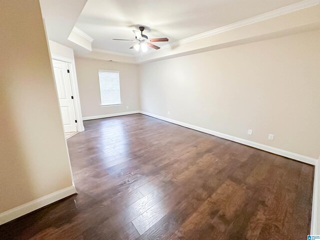 empty room with dark hardwood / wood-style floors, ornamental molding, a raised ceiling, and ceiling fan