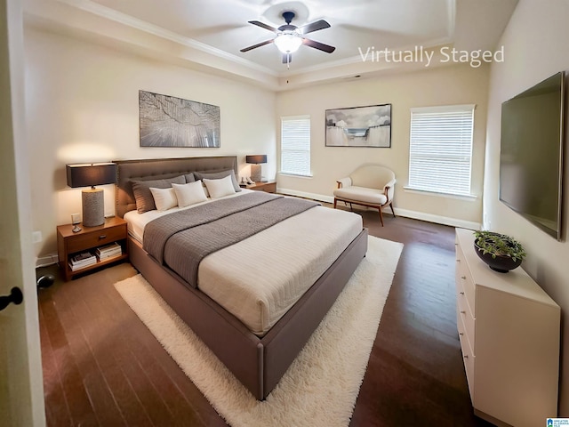 bedroom with crown molding, dark wood-type flooring, a raised ceiling, and ceiling fan