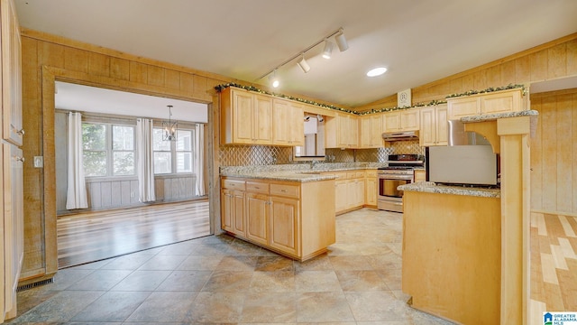 kitchen featuring vaulted ceiling, pendant lighting, wooden walls, stainless steel gas range oven, and light brown cabinets