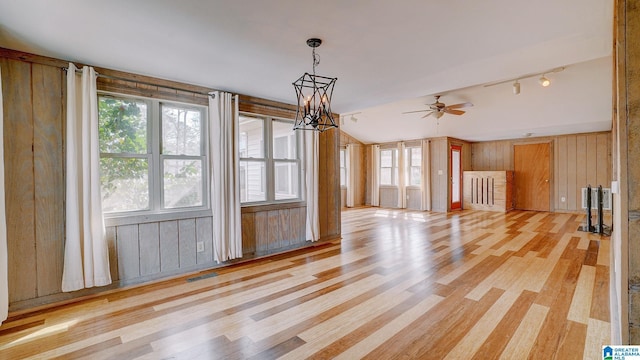 unfurnished living room featuring wood walls, lofted ceiling, ceiling fan with notable chandelier, and light wood-type flooring