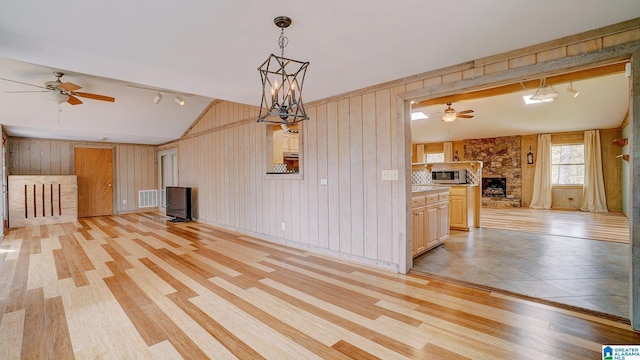 unfurnished living room featuring vaulted ceiling, rail lighting, ceiling fan with notable chandelier, and light hardwood / wood-style floors