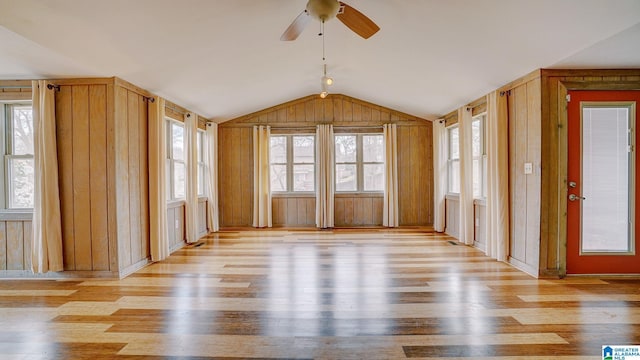 interior space with light hardwood / wood-style flooring, vaulted ceiling, wood walls, and plenty of natural light