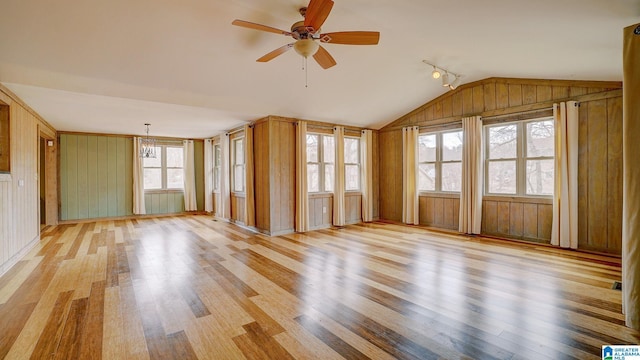 interior space with lofted ceiling, wooden walls, ceiling fan with notable chandelier, and light wood-type flooring