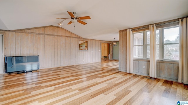 unfurnished living room with lofted ceiling, wooden walls, ceiling fan with notable chandelier, and light wood-type flooring