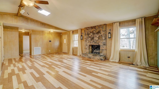 unfurnished living room with a fireplace, wood walls, lofted ceiling, light hardwood / wood-style floors, and ceiling fan