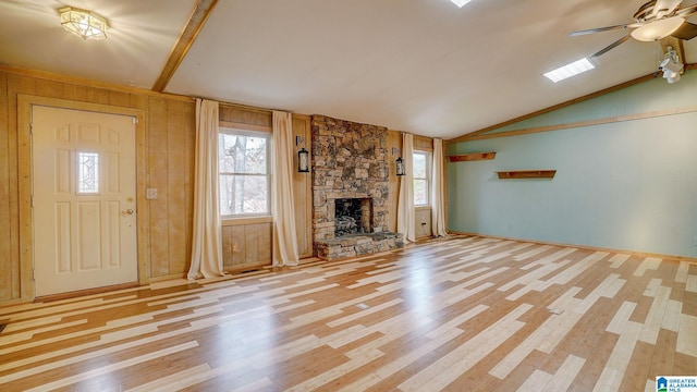 unfurnished living room with a stone fireplace, vaulted ceiling, ceiling fan, and light wood-type flooring