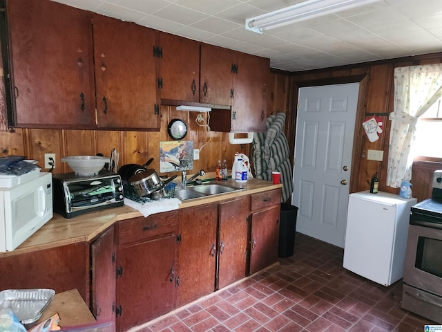 kitchen featuring electric stove, sink, refrigerator, and wood walls