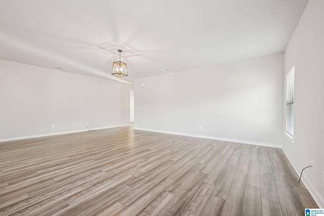 spare room featuring a chandelier and light hardwood / wood-style floors