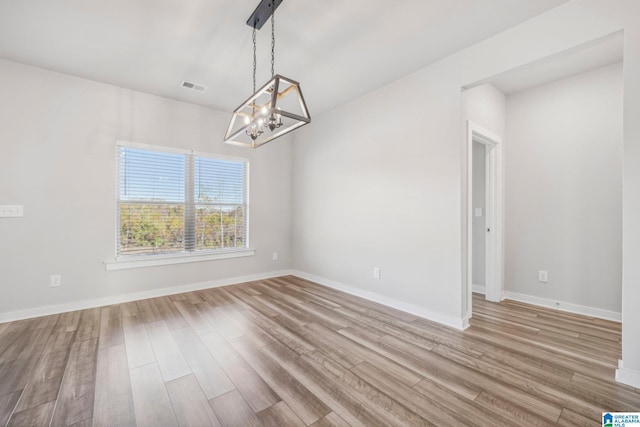 unfurnished room featuring a notable chandelier and light hardwood / wood-style floors