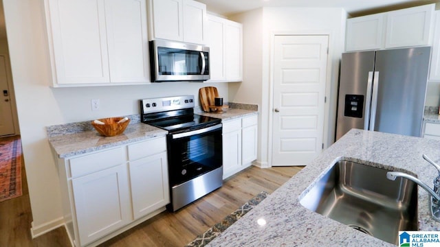 kitchen with sink, white cabinets, light stone counters, light hardwood / wood-style floors, and stainless steel appliances