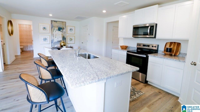 kitchen featuring sink, white cabinetry, light stone counters, appliances with stainless steel finishes, and a kitchen island with sink