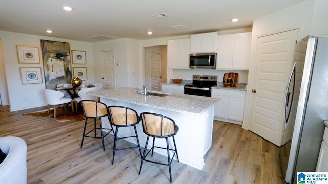 kitchen featuring sink, white cabinetry, stainless steel appliances, light stone counters, and a center island with sink