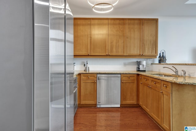 kitchen with sink, light stone counters, decorative light fixtures, stainless steel appliances, and hardwood / wood-style floors