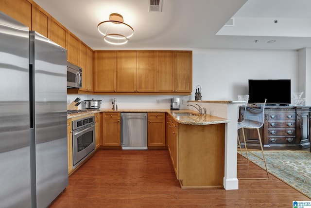 kitchen with sink, dark hardwood / wood-style flooring, kitchen peninsula, stainless steel appliances, and light stone countertops