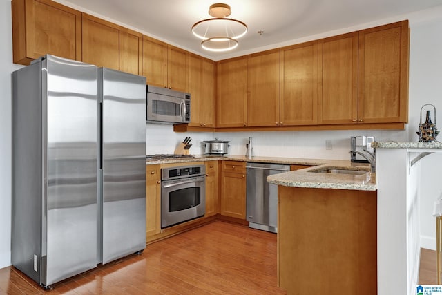 kitchen with sink, light wood-type flooring, stainless steel appliances, light stone countertops, and backsplash