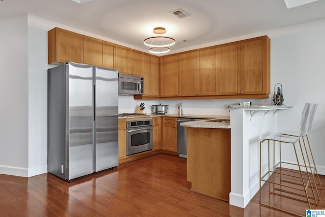 kitchen featuring stainless steel appliances, dark hardwood / wood-style floors, a breakfast bar area, and kitchen peninsula