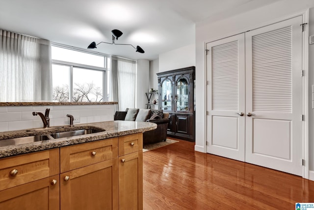 kitchen with sink, backsplash, light wood-type flooring, and stone counters