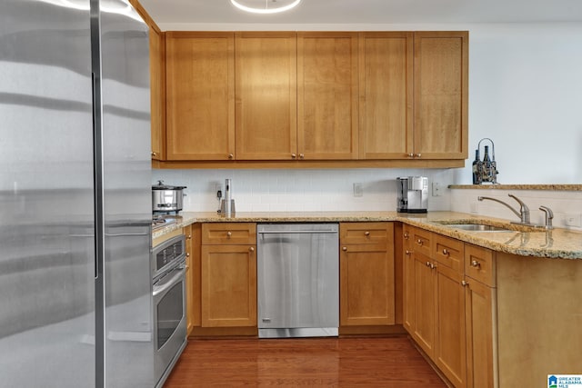 kitchen with appliances with stainless steel finishes, tasteful backsplash, sink, dark hardwood / wood-style flooring, and light stone counters