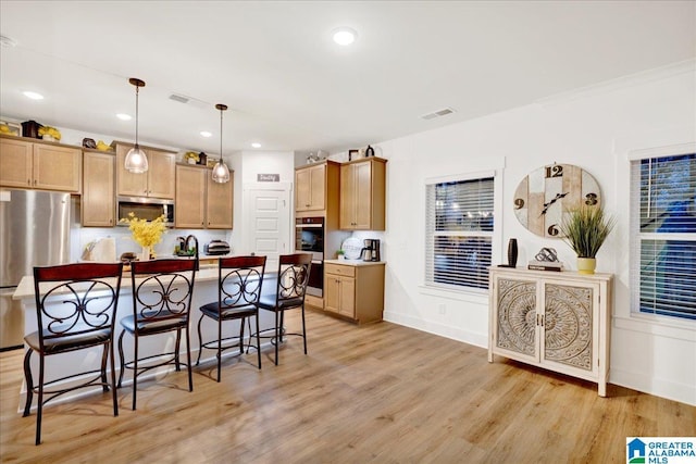 kitchen featuring a breakfast bar area, appliances with stainless steel finishes, a center island with sink, decorative light fixtures, and light wood-type flooring