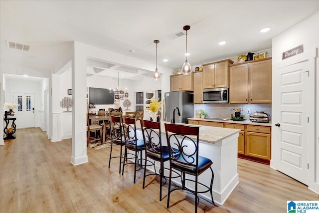 kitchen featuring appliances with stainless steel finishes, decorative light fixtures, a kitchen island with sink, and light hardwood / wood-style flooring