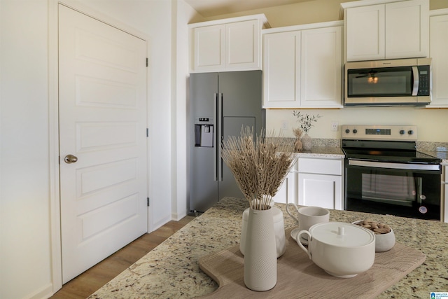 kitchen with white cabinetry, stainless steel appliances, light stone countertops, and light hardwood / wood-style flooring