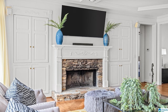 living room with a stone fireplace, wood-type flooring, and ornamental molding