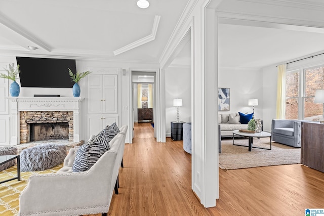 living room with crown molding, a stone fireplace, and light hardwood / wood-style flooring