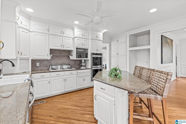 kitchen with a breakfast bar, sink, white cabinets, light stone counters, and stainless steel appliances