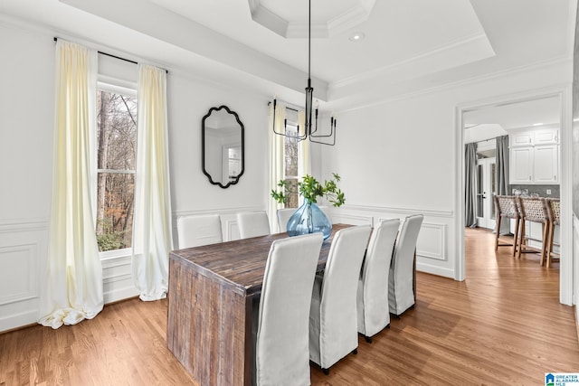 dining area featuring crown molding, a raised ceiling, an inviting chandelier, and light hardwood / wood-style flooring