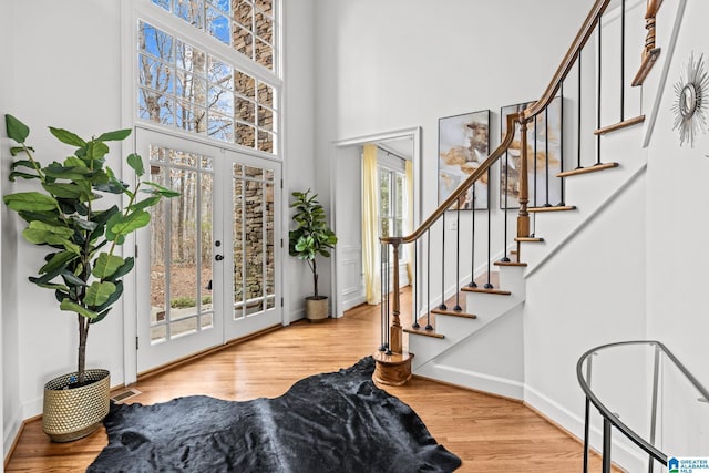 foyer with french doors, a towering ceiling, and light wood-type flooring